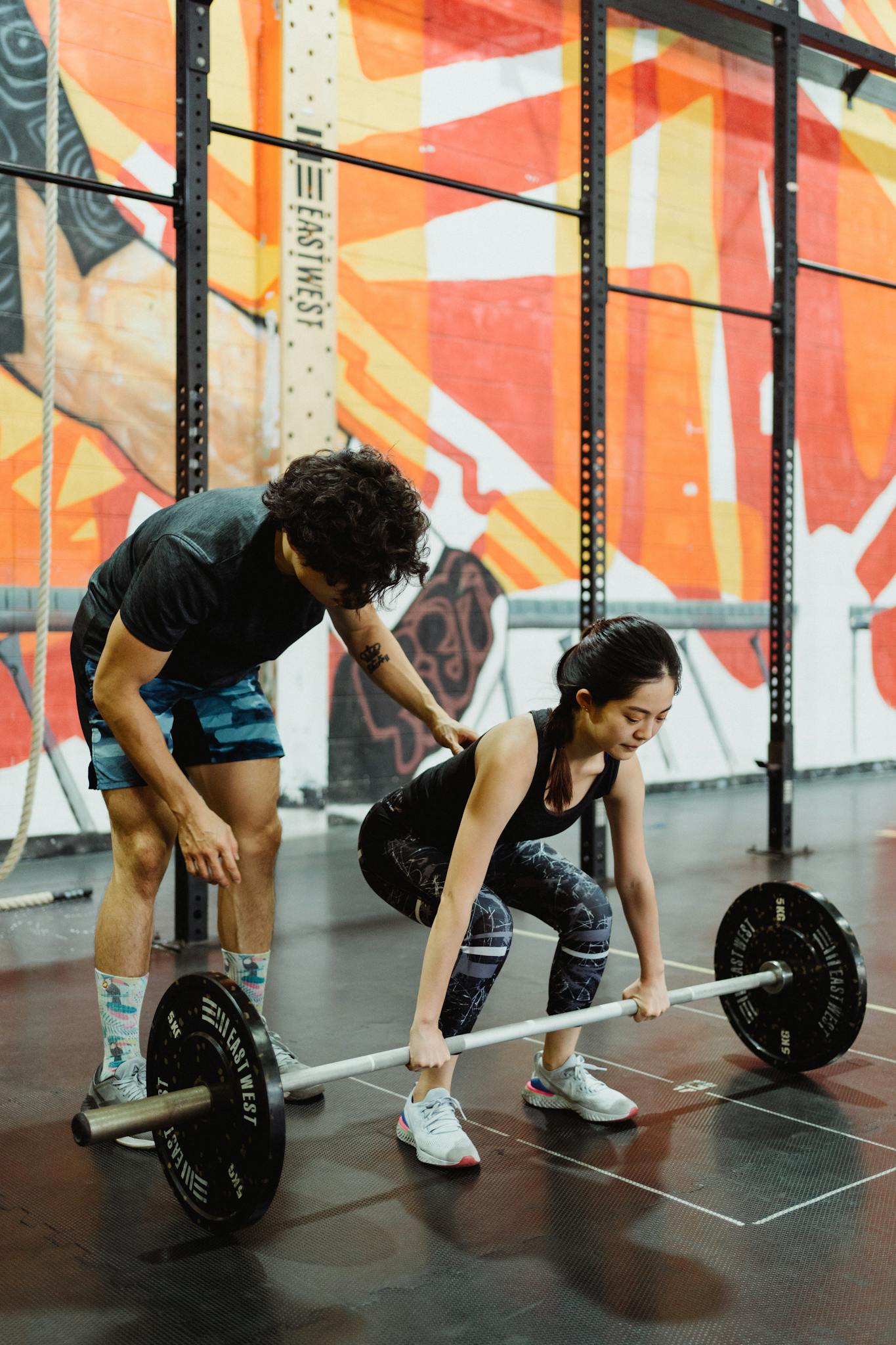 A female weightlifter getting coached on lifting techniques in an indoor gym.