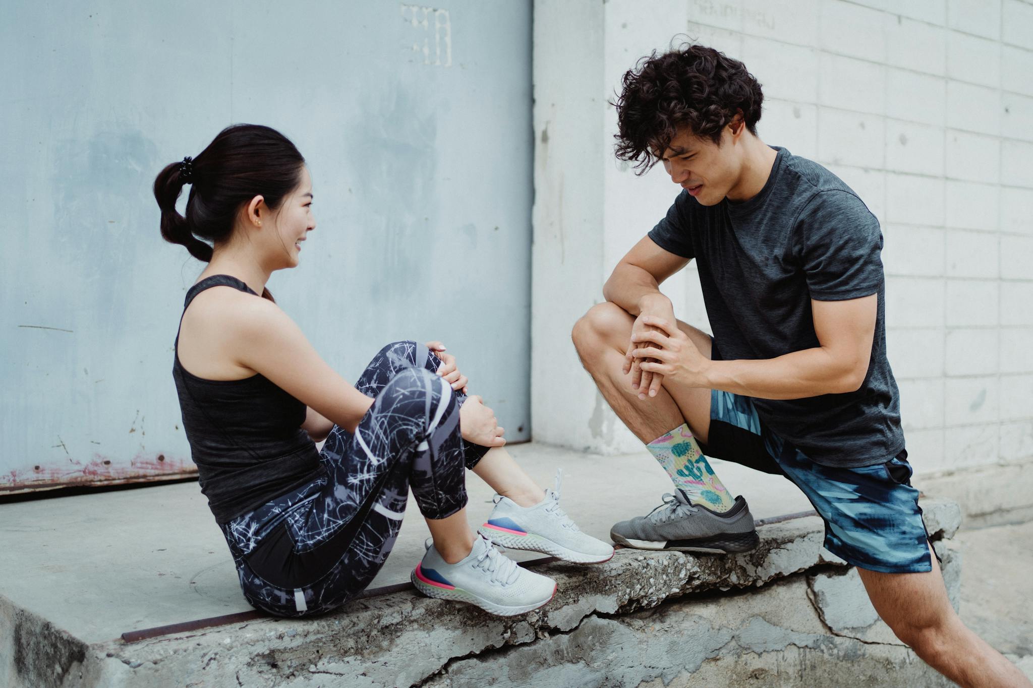 Two young adults in sportswear stretching outdoors, promoting fitness and health.